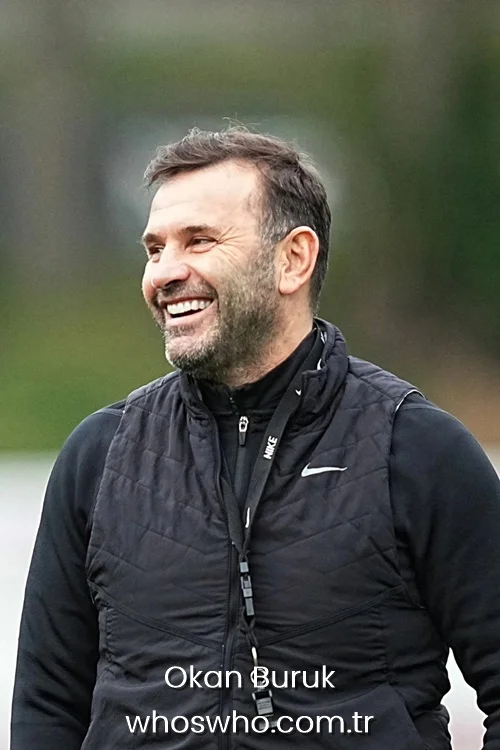 Football coach Okan Buruk laughing during a team training session on the pitch.