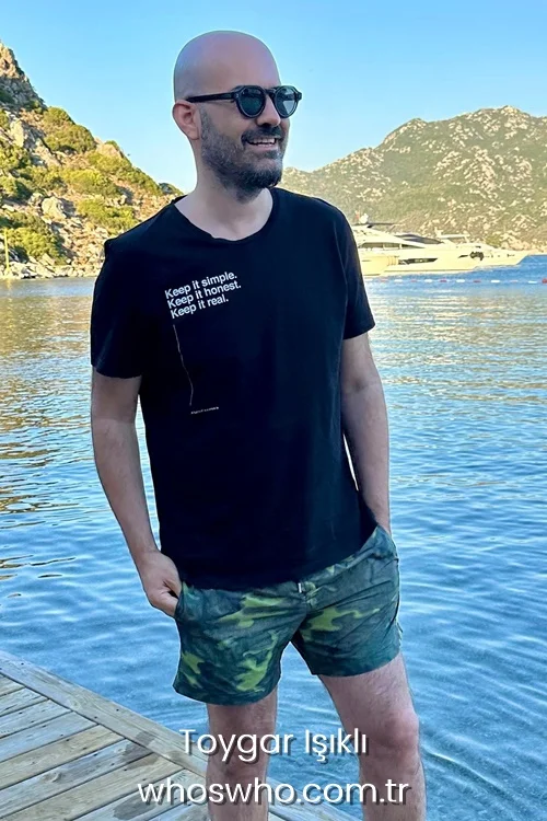 Turkish music composer Toygar Isikli wearing a black t-shirt and sunglasses while standing on a wooden pier by the sea during summer vacation 