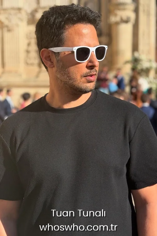 Actor Tuan Tunali wearing white sunglasses and a black t-shirt outdoors.